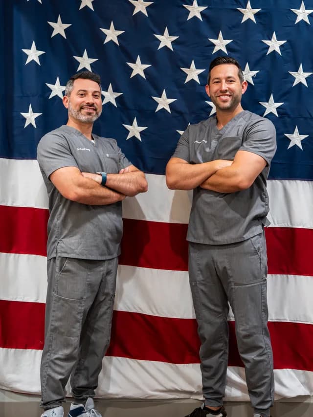 Dr. Wolf and Dr. Honig, the veteran-owned doctors of Illumination Dentistry, standing in front of an American flag in support of local Veteran charities