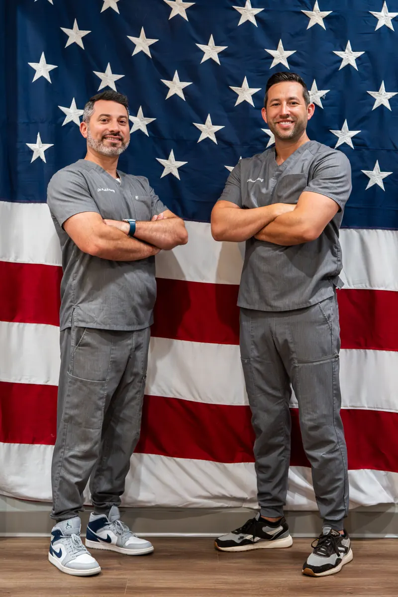 Dr. Wolf and Dr. Honig, the veteran-owned doctors of Illumination Dentistry, standing in front of an American flag in support of local Veteran charities